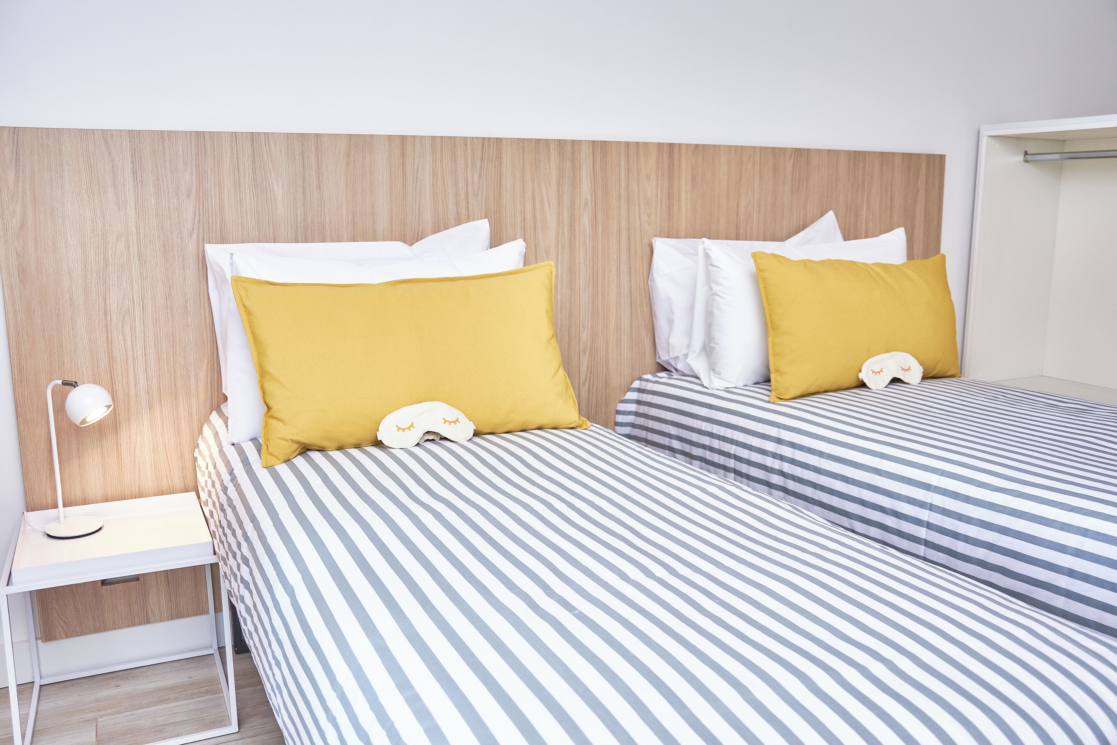 A hotel room with two beds, a bedside table with a lamp, and a wooden headboard.