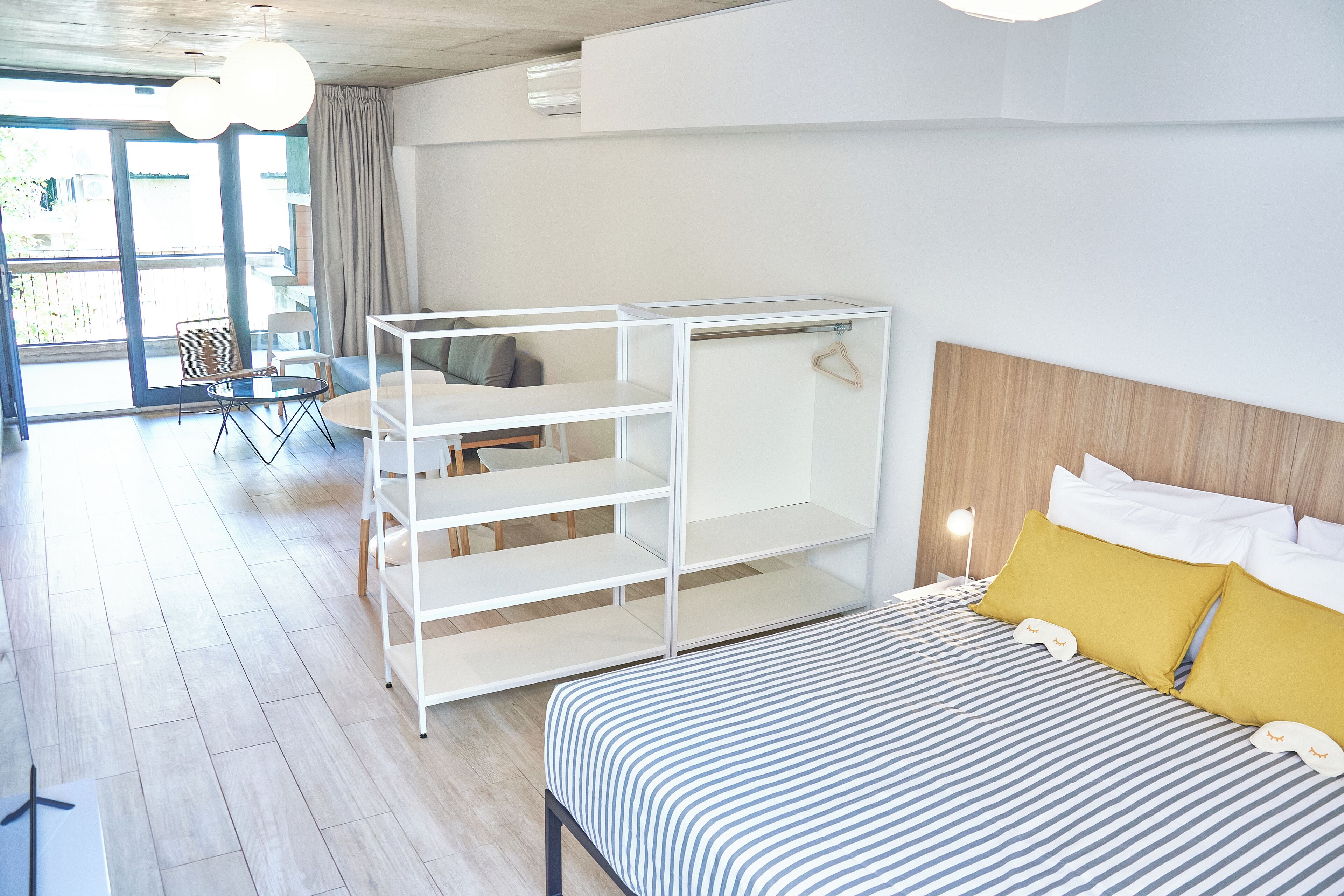 Una habitación de hotel moderna con una cama, un armario blanco, una mesita pequeña y una silla.