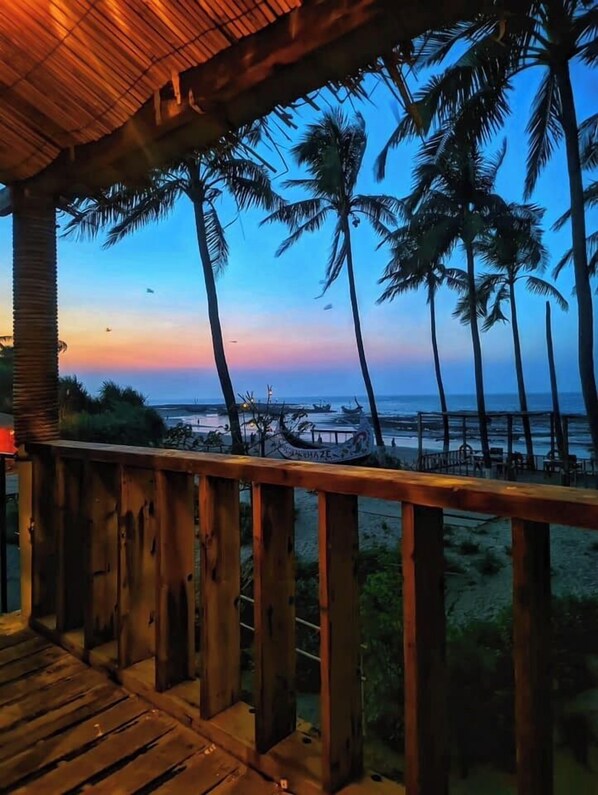 Una terraza de madera con vistas al océano y palmeras al atardecer.