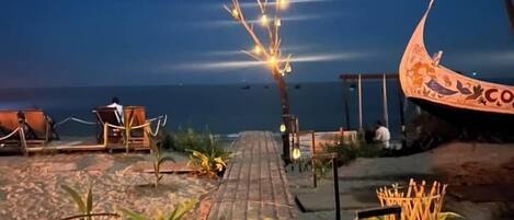 A wooden pathway leading to a beach area with lounge chairs and a decorative boat structure.