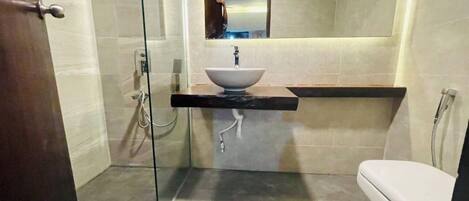 A bathroom with a glass shower enclosure, a white sink with a marble countertop, and a toilet.