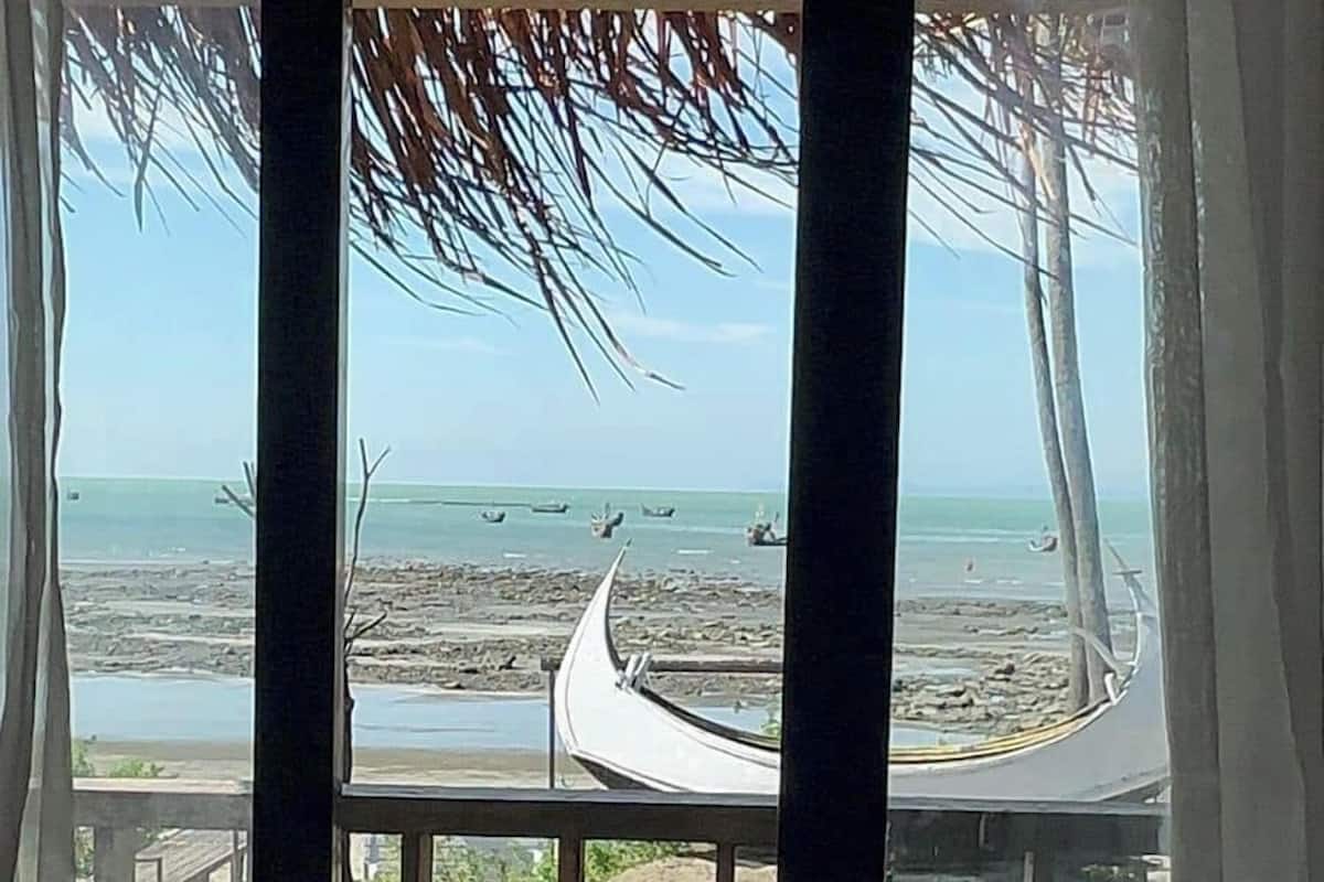 Eine Holzterrasse mit einem Reetdach, mit Blick auf einen Strand mit Booten und einem gewundenen Pfad.
