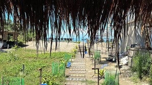 Un sentier bordant la plage qui mène à une construction recouverte d’un toit de chaume.