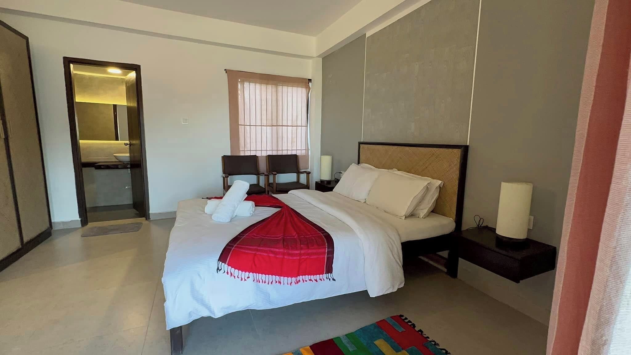 Une chambre d’hôtel moderne avec un grand lit, deux tables de chevet, une commode, une fenêtre avec des rideaux et un miroir.