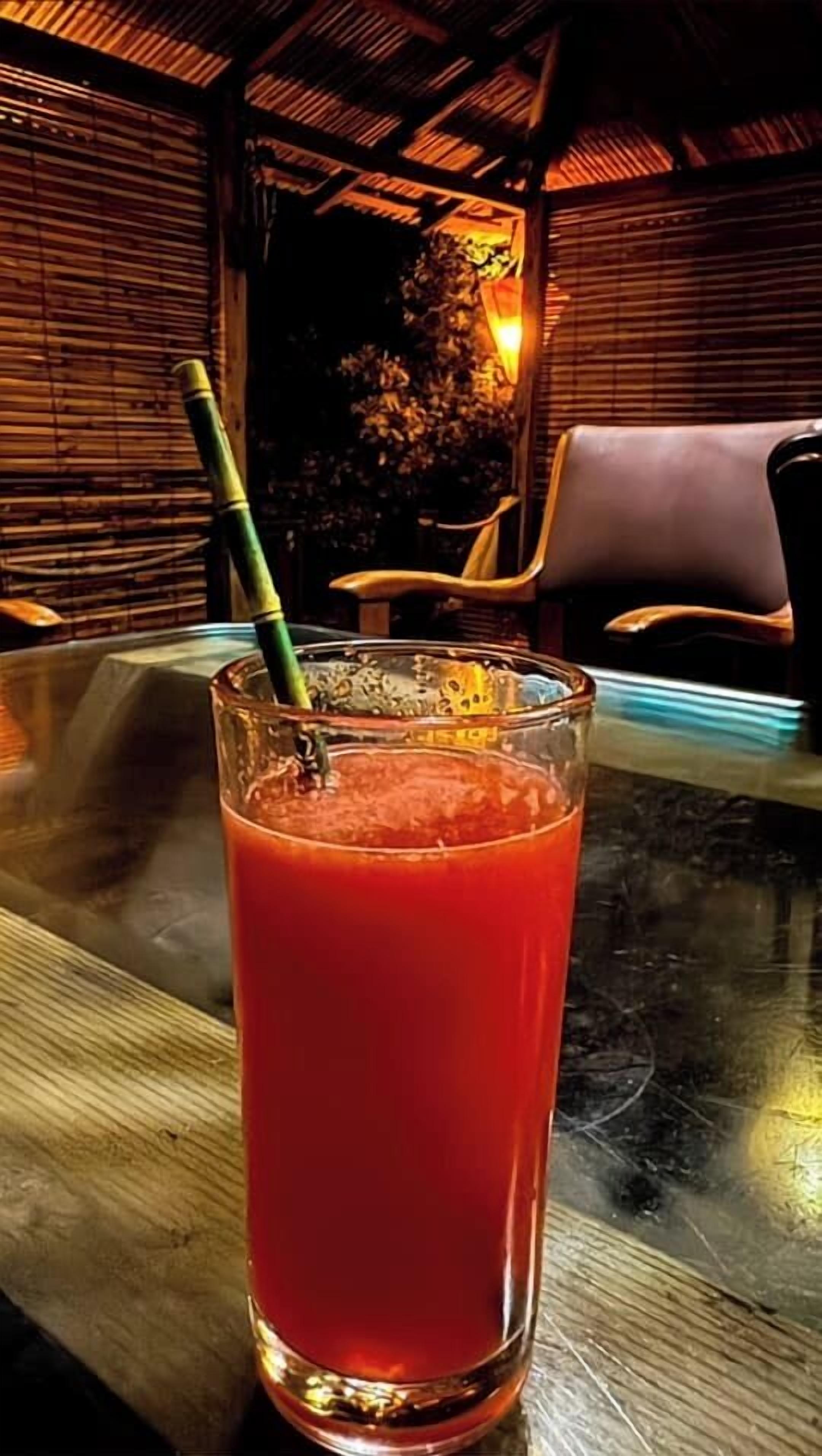 Un vaso de bebida roja con una pajita sobre una mesa.