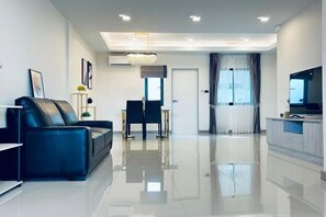 A modern living room with a black leather sofa, a dining table with chairs, a chandelier, and a flat-screen TV on a wooden cabinet. - Yunman Vacation Villa Pattaya (Pattaya)