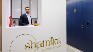 A reception area with a man standing behind a counter, a blue door, and the text "Shamika Luxury Rooms". - Shamika Luxury Rooms (Montecorvino Pugliano)