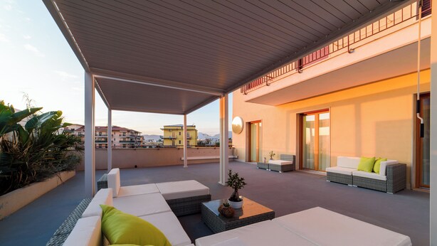 A covered outdoor seating area with white sofas and cushions, a potted plant, and a view of the cityscape in the background. - Shamika Luxury Rooms (Montecorvino Pugliano)
