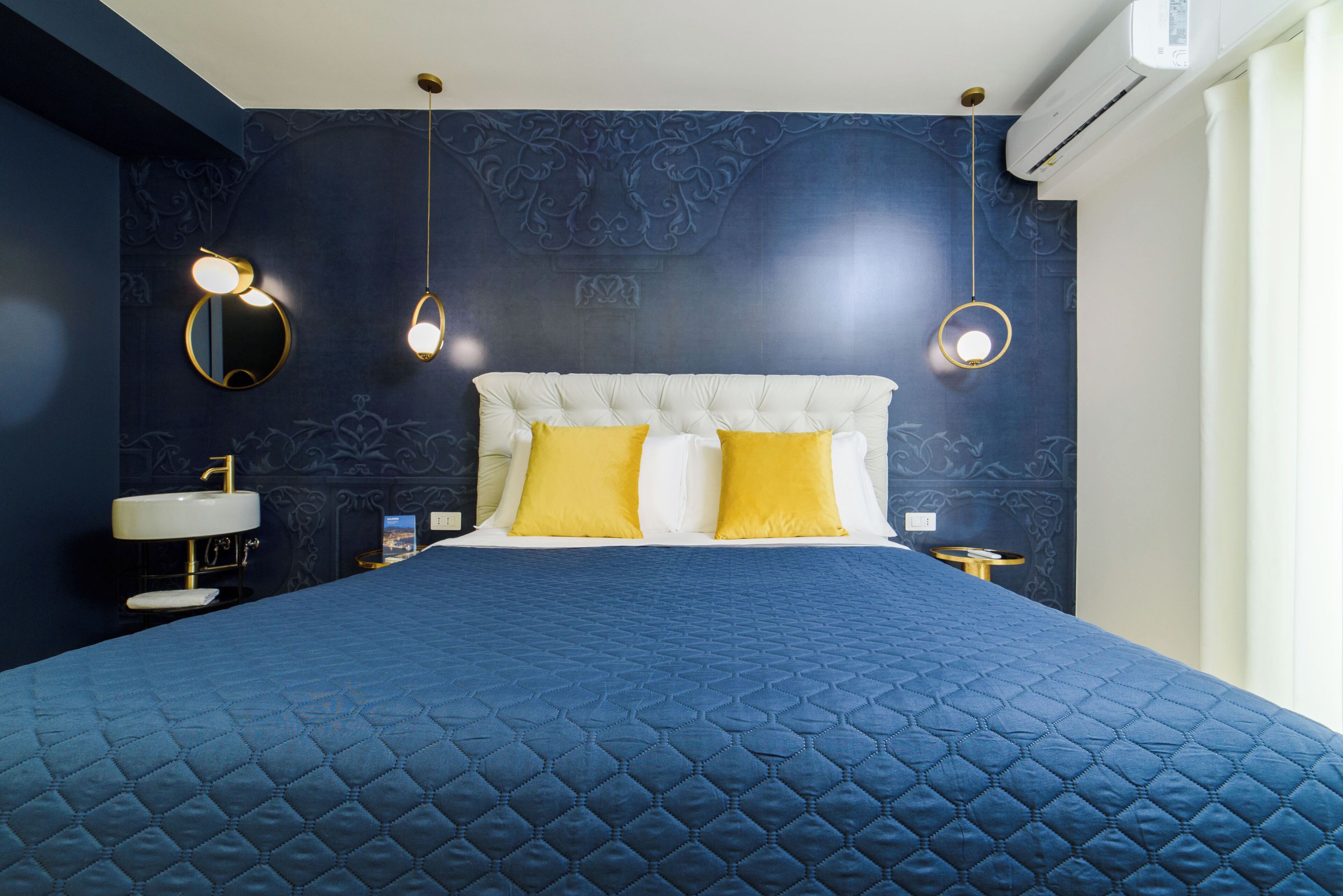 A bedroom with a large bed, two bedside tables, a round mirror, and a wall-mounted air conditioner.