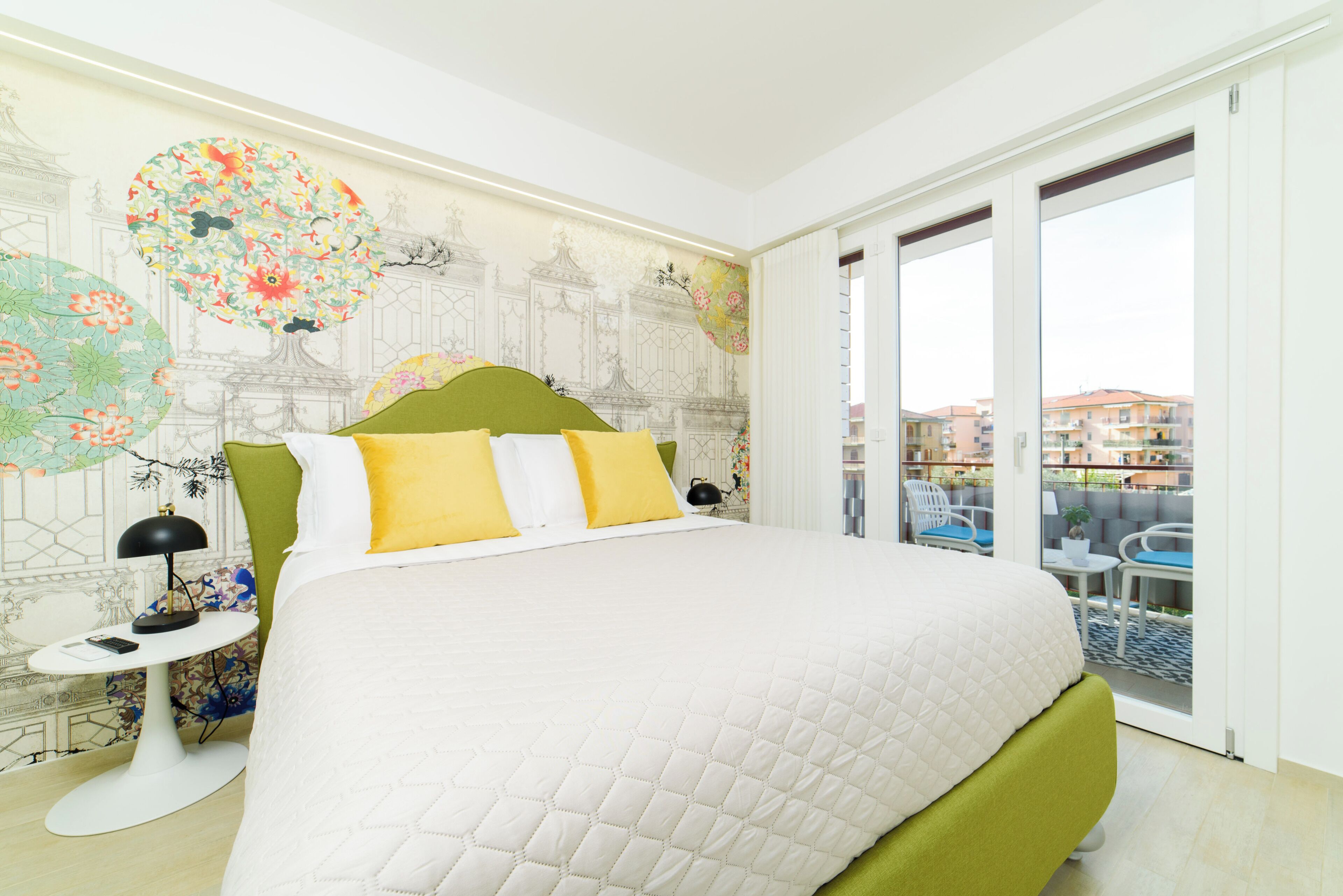 Ein Hotelzimmer mit einem großen Bett, einem kleinen Beistelltisch, einem dekorativen Wandbild und einem Balkon mit Sitzgelegenheit.