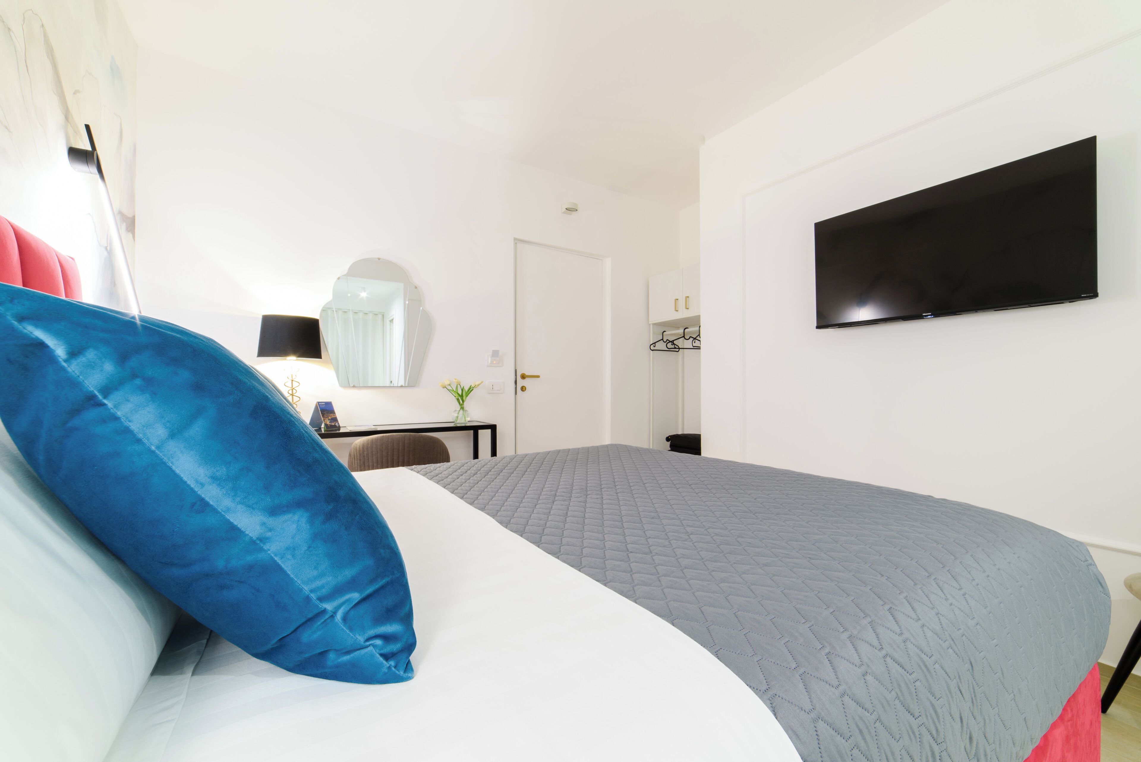 A hotel room with a bed, a desk, a chair, a TV mounted on the wall, and a door.