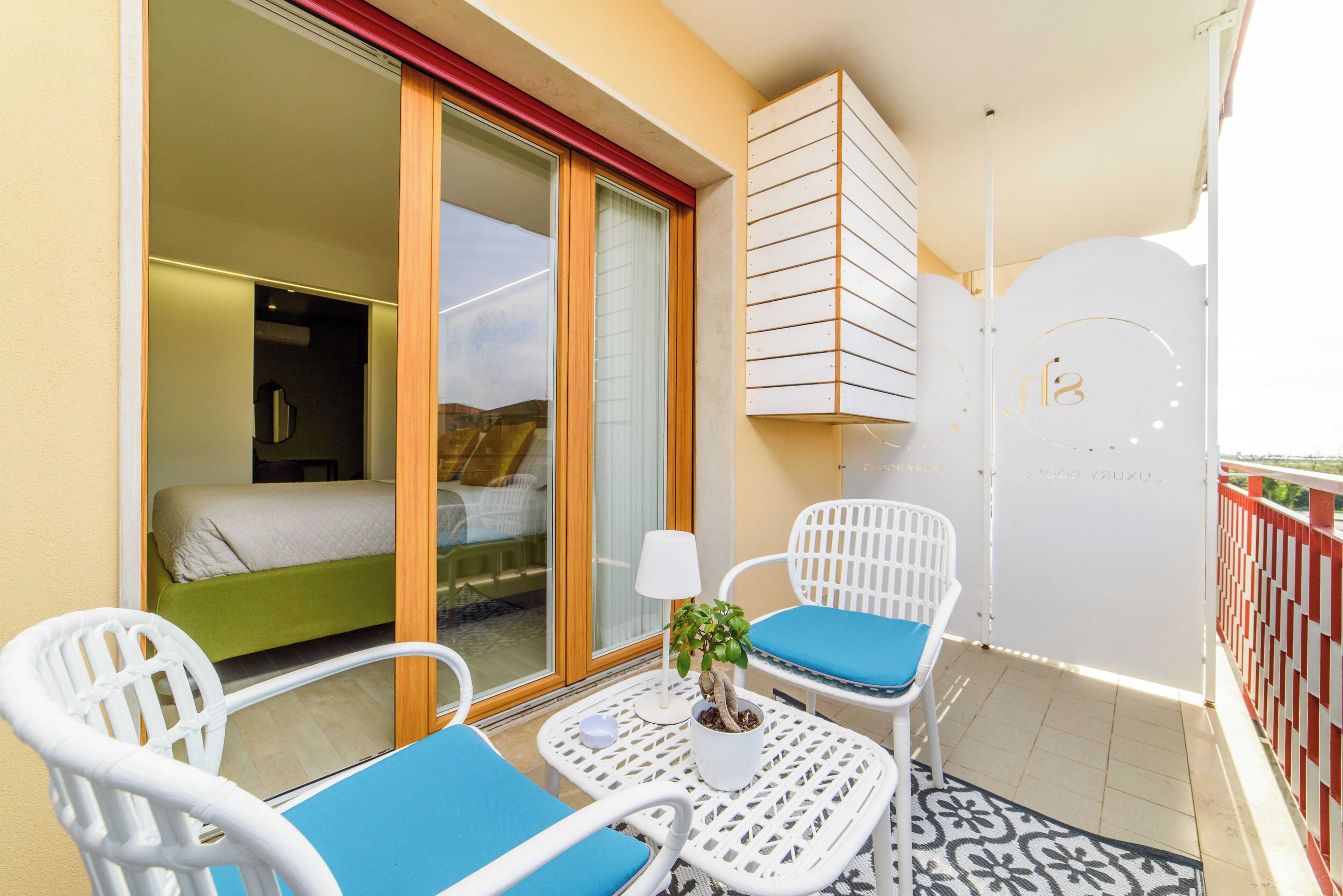 A balcony with white wicker furniture, a small table with a lamp, and a potted plant.