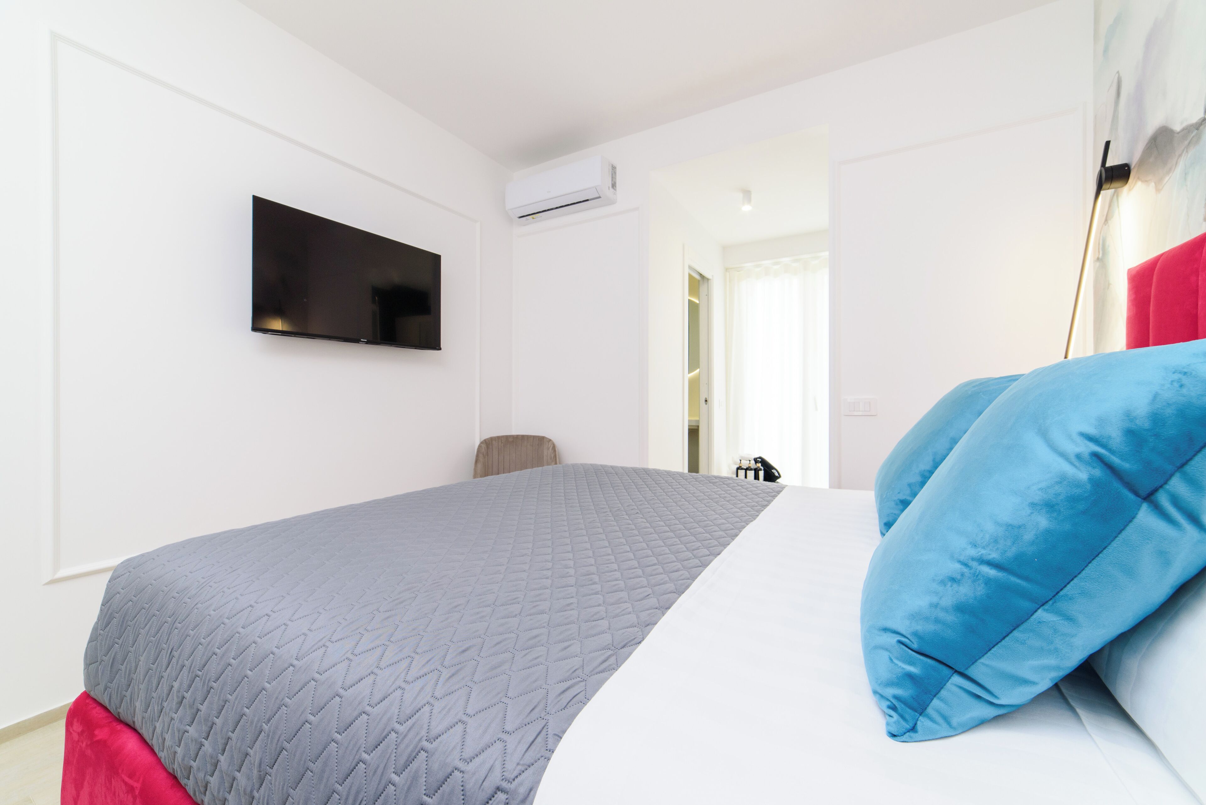 A bedroom with a bed, a flat-screen TV mounted on the wall, and an air conditioning unit.