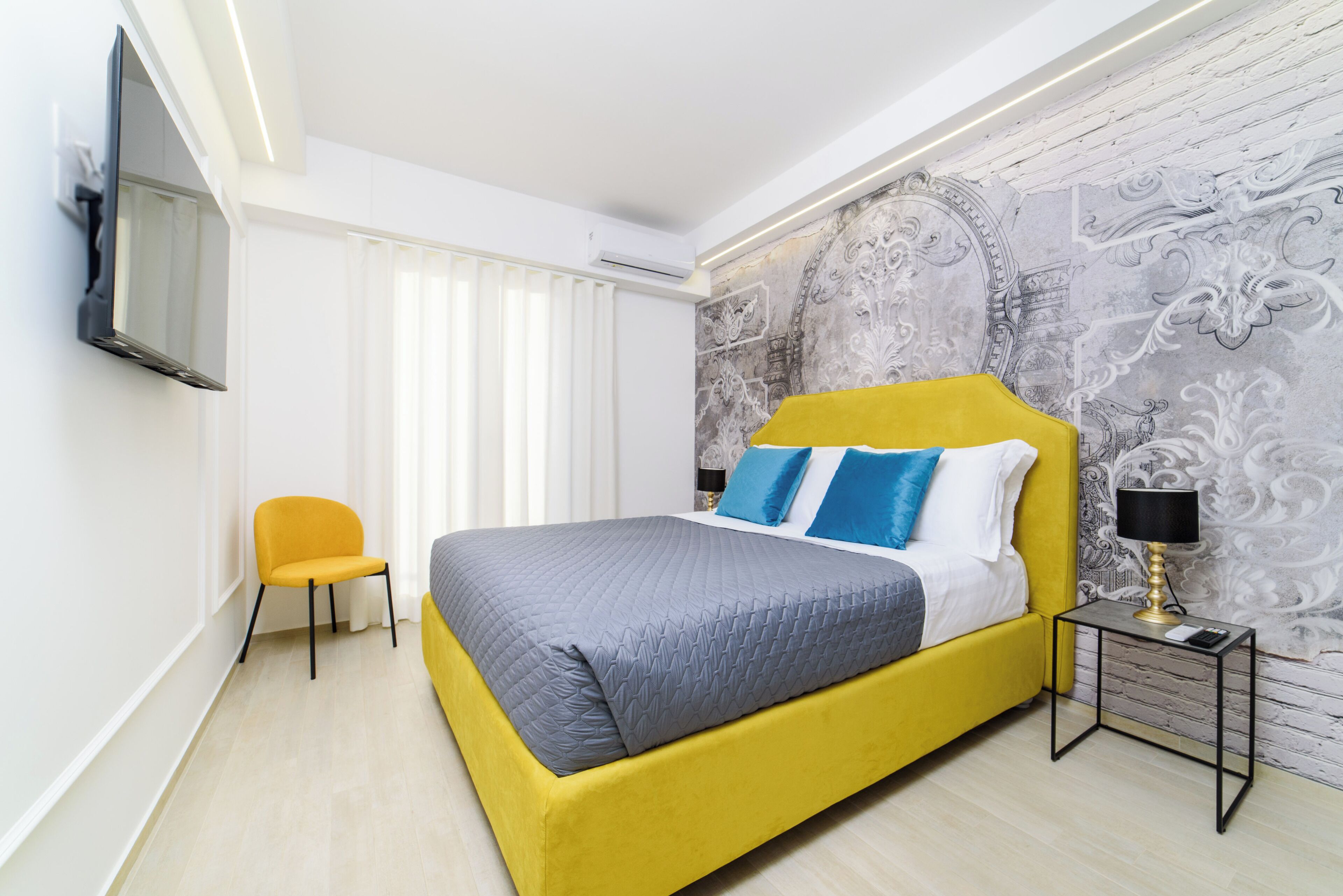 Une chambre à coucher moderne avec un lit jaune, une petite table de chevet, une chaise et un mur décoratif.