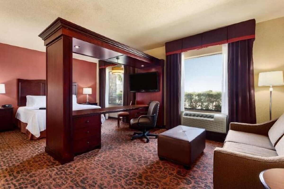 Une chambre d’hôtel avec un lit à baldaquin, un bureau, une chaise, un canapé, une télévision et une grande fenêtre.