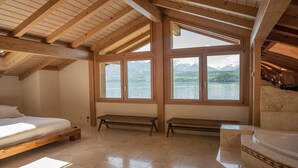 Una camera da letto con soffitto in legno, ampie finestre, un letto, una panca e una vasca da bagno.