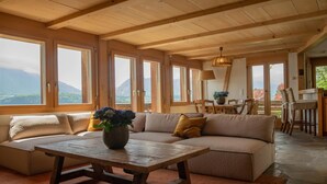 Un soggiorno accogliente con soffitto in legno, ampie finestre, un divano, un tavolino da caffè e una zona pranzo.