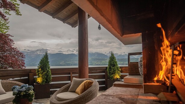 Una zona relax esterna accogliente con mobili in vimini, un elemento decorativo a forma di fuoco e vista sulle montagne.