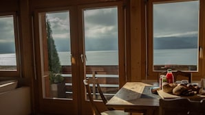Un'area pranzo in legno con un tavolo apparecchiato per due, con vista su un lago e montagne sullo sfondo.