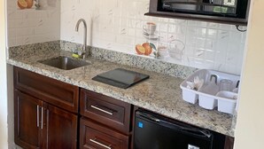 A kitchen with a granite countertop, stainless steel sink, dark wooden cabinets, a black dishwasher, and a microwave. - Studio bungalow WiFi/ Hot Water in flourishing Drax Hall (Saint Ann's Bay)