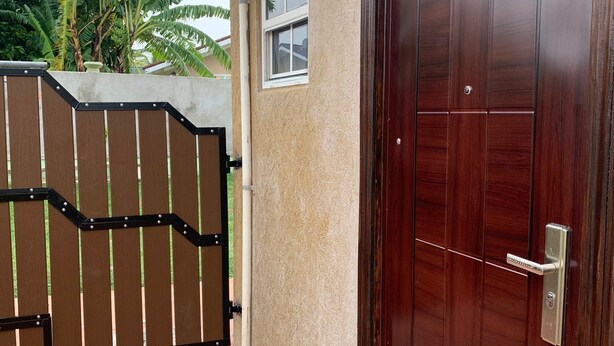 A wooden door with a metal handle, a gated entrance, and a small window above the door. - Studio bungalow WiFi/ Hot Water in flourishing Drax Hall (Saint Ann's Bay)