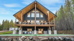A two-story log cabin with a balcony, stone foundation, and a view of a forest. - Midnight Pines Lodge+HotTub+Cent AC+20mYellowstone (Island Park)