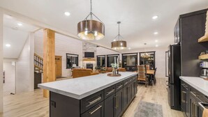 A modern kitchen with a large island, dark cabinetry, and pendant lighting. - Midnight Pines Lodge+HotTub+Cent AC+20mYellowstone (Island Park)