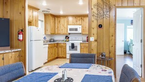 A cozy cabin-style room with wooden walls, a kitchenette, a dining area with a table and chairs, and a bed with a floral bedspread. - Treetop Villa, Charming cottage on 100 acres with WiFi and AC in serene Mariposa (Mariposa)