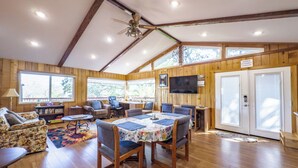 A spacious room with wooden walls and a sloped ceiling, featuring a dining table with chairs, a sofa, and a television mounted on the wall. - Treetop Villa, Charming cottage on 100 acres with WiFi and AC in serene Mariposa (Mariposa)