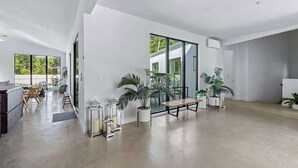 A spacious, modern interior with a large open-plan layout, featuring a dining area, seating area with potted plants, and large windows providing natural light. - Juniper Presents: Fab Vacay Home, Pool, Walk to Lake Michigan Beach (Michigan City)