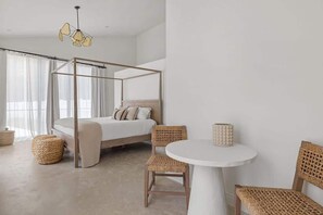 A bedroom with a four-poster bed, wicker chairs, a round table, and a hanging light fixture.