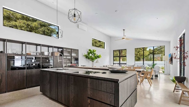 A modern kitchen with a large island, dark wood cabinetry, and a view of greenery through a window. - Juniper Presents: Fab Vacay Home, Pool, Walk to Lake Michigan Beach (Michigan City)
