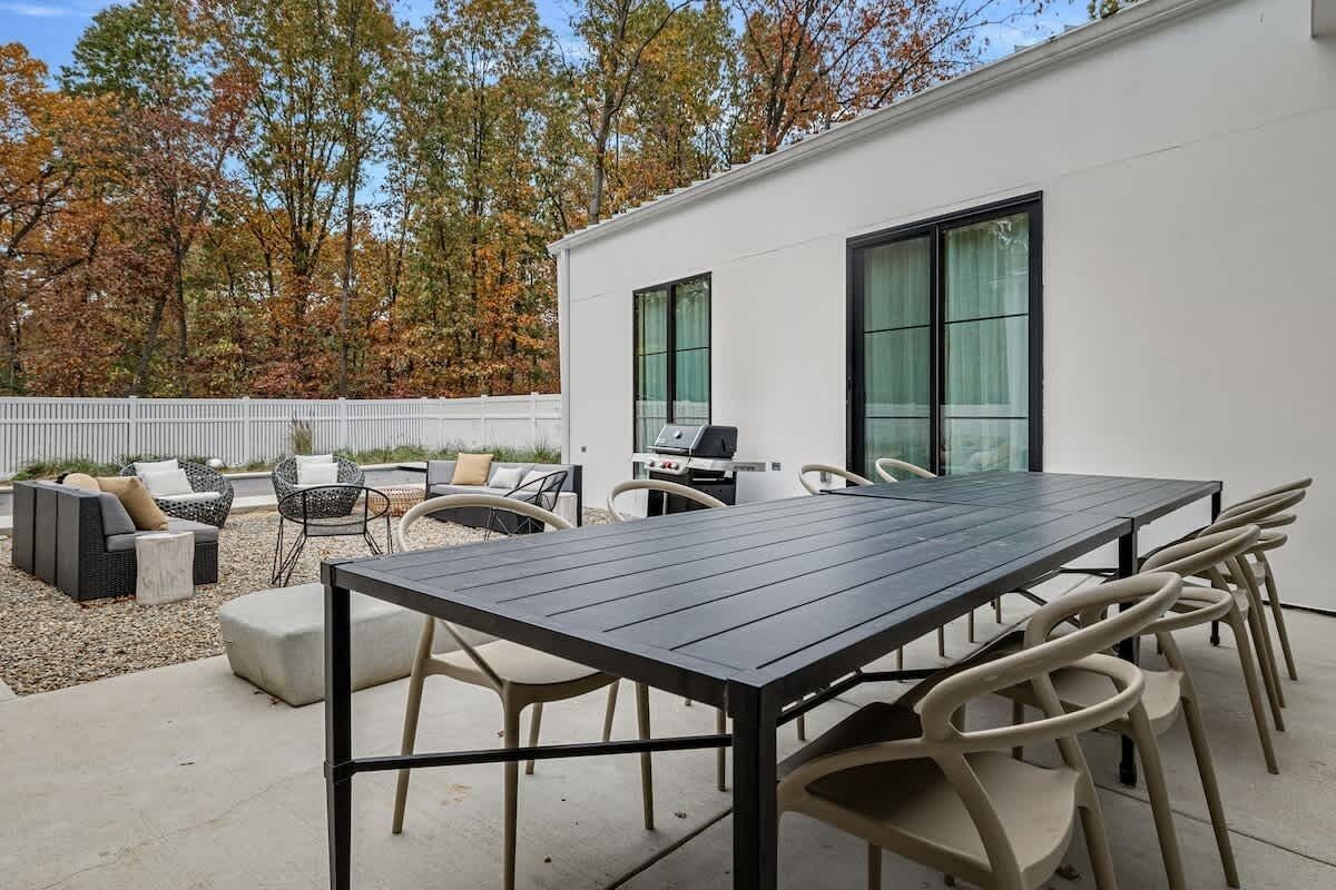 A modern outdoor patio with a dining table, chairs, and a grill.