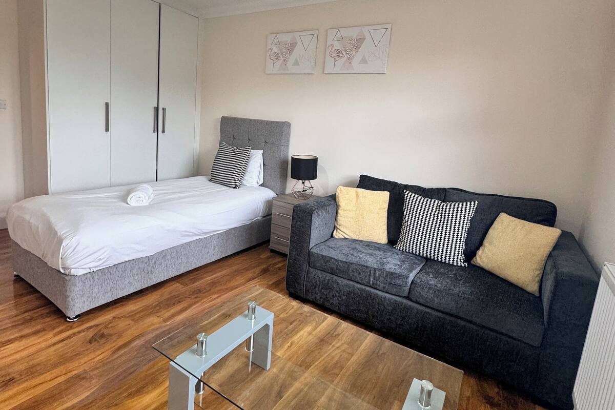 A modern bedroom with a bed, a sofa, a glass coffee table, and a wardrobe.