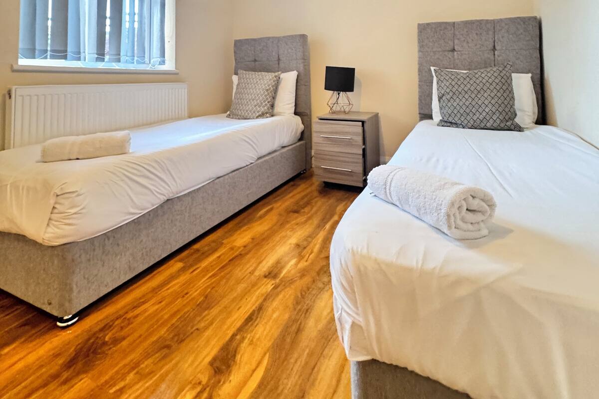 A bedroom with two beds, a nightstand, a lamp, and artwork on the wall.