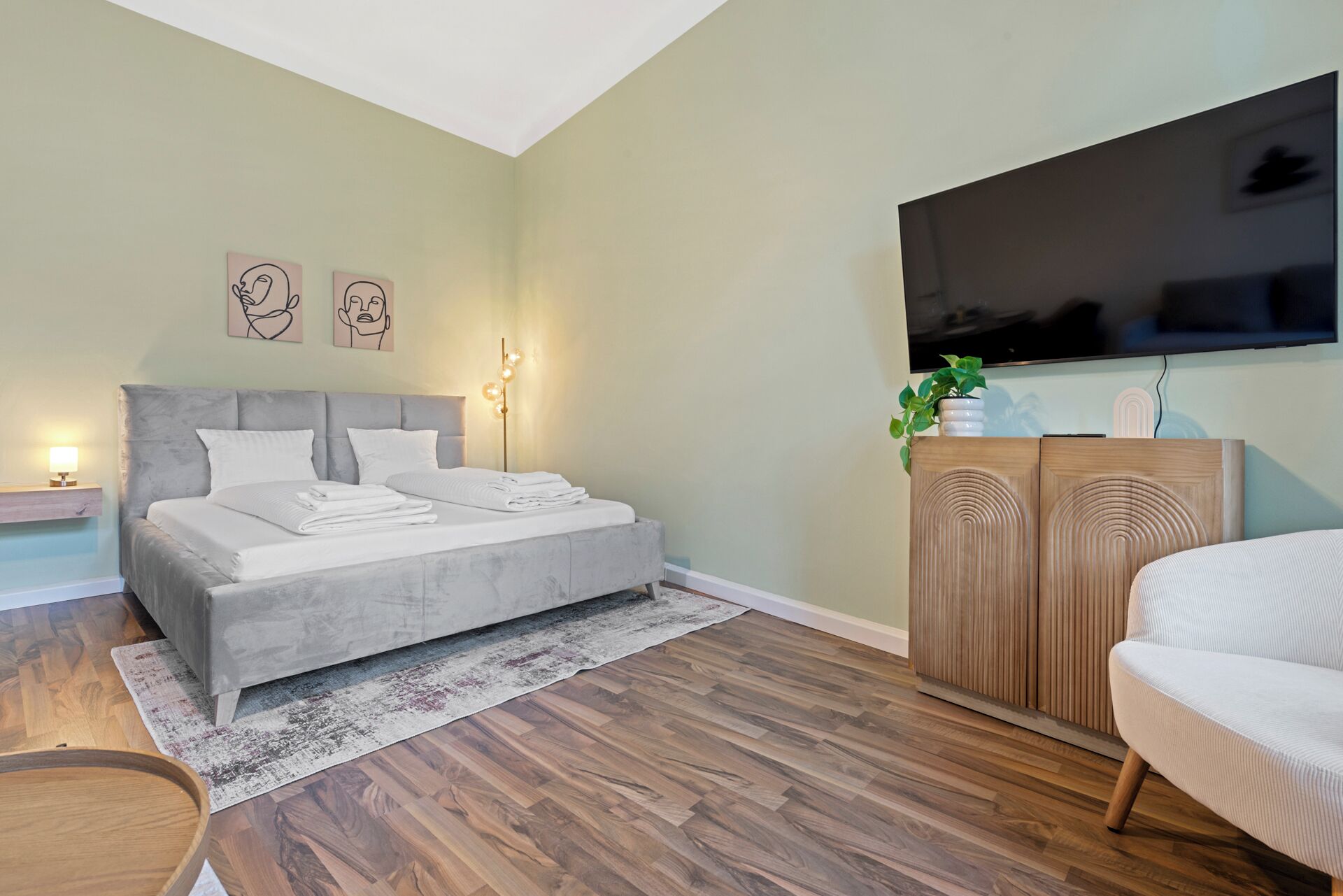 A modern bedroom with a large bed, a TV mounted on the wall, and a wooden cabinet.