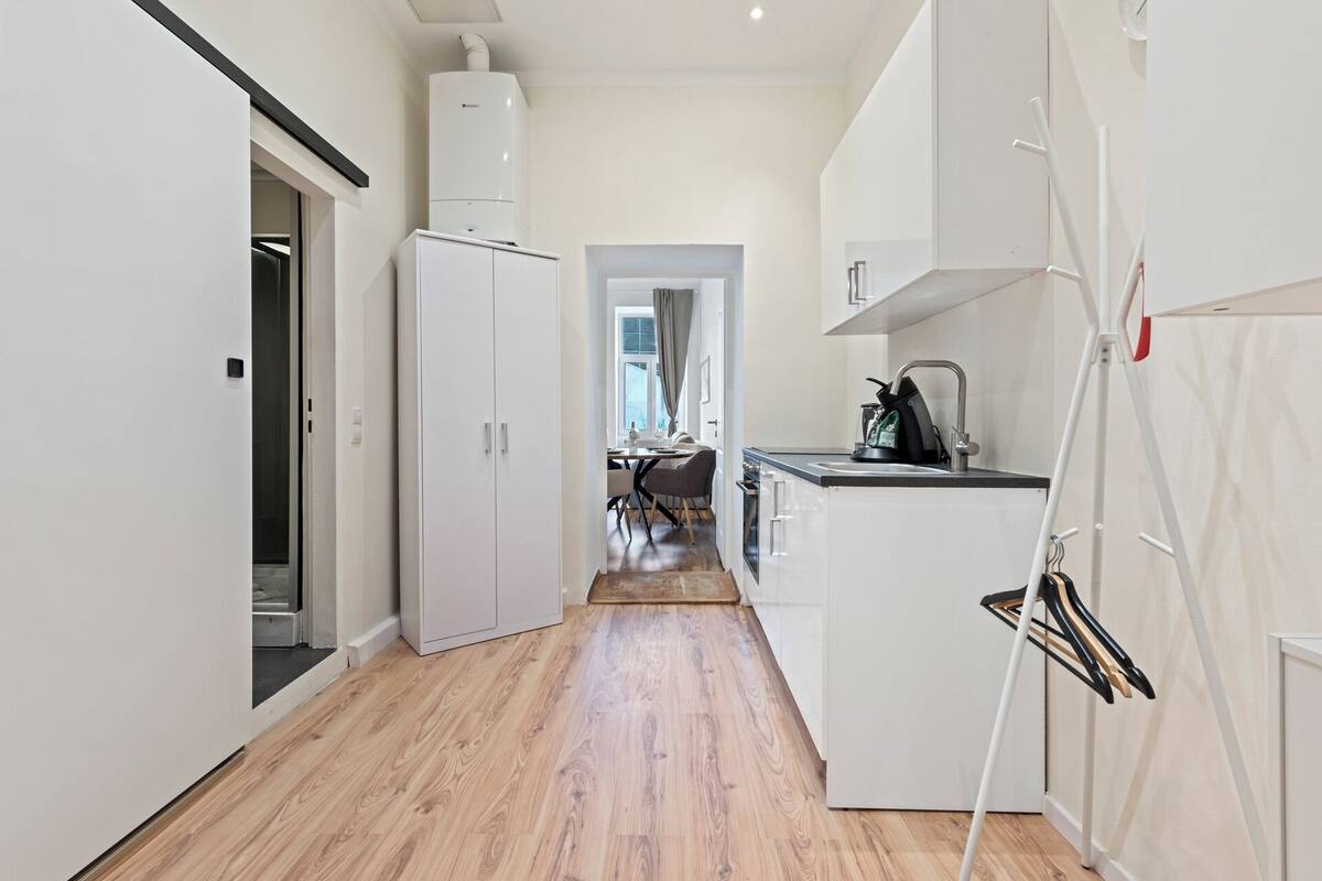 A narrow hallway with a kitchen area on the right, featuring white cabinets, a sink, and a stove.