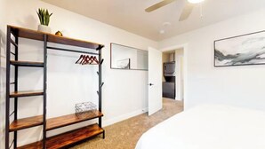 A hotel room with a bed, a wooden shelf unit, a ceiling fan, and a door leading to a kitchen area.