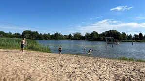 Une plage de sable avec un lac, des arbres et une jetée où se trouvent des personnes.