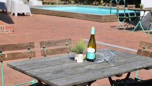 Une terrasse extérieure avec une table en bois, une bouteille de vin, une petite plante en pot et un verre.