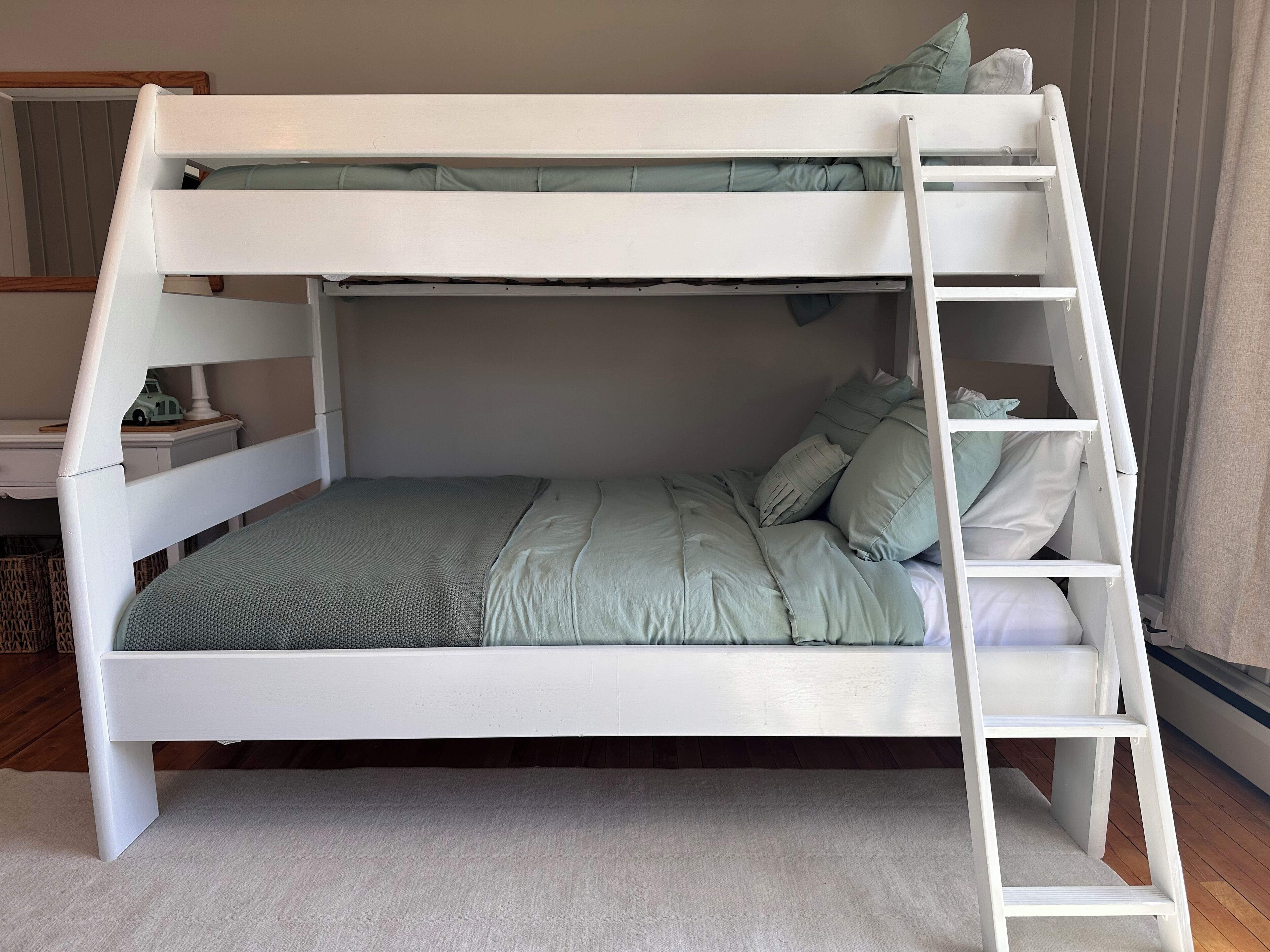A bunk bed with a ladder, green bedding, and pillows.