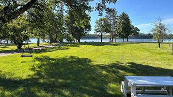 A grassy park area with a swing set, picnic table, and trees.