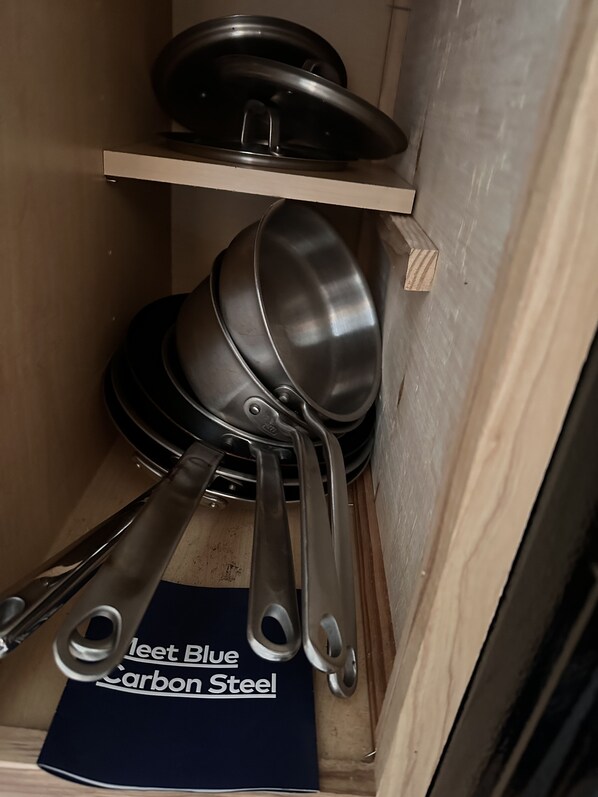 Una cocina con ollas y sartenes de acero inoxidable guardadas en un estante de madera.