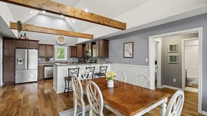 A spacious kitchen with wooden beams, a central island, and a dining area with white chairs. - 5 BDRM Dog Friendly, Lake Access Getaway w/Playground, Fire Pit & more (Louisa)