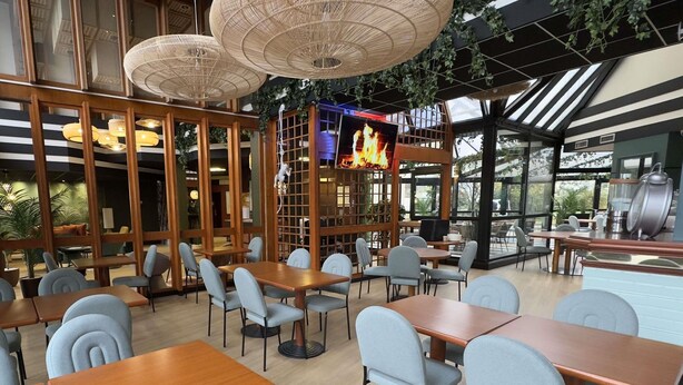A restaurant with wooden tables and chairs, large windows, and hanging rattan lamps.