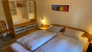Quarto com cama, guarda-roupa de madeira, cadeira e mesa de cabeceira com abajur.