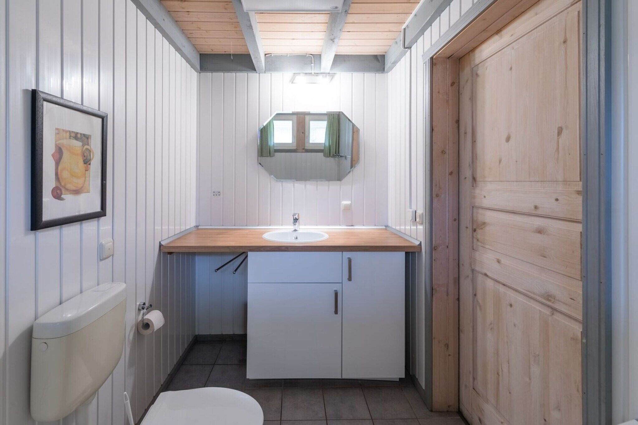 A compact bathroom with a wooden vanity, a toilet, and a mirror above the sink.
