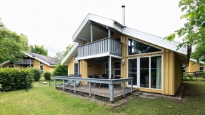 Una casa moderna con fachada de madera, un balcón y una zona de estar exterior cubierta.