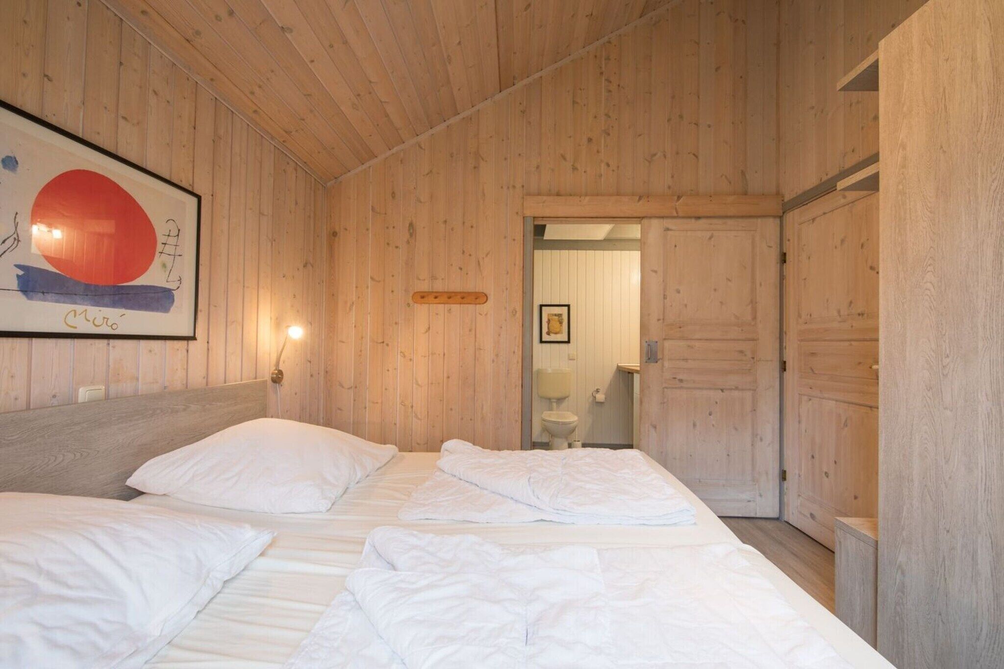A wooden room with a bed, a framed artwork, and a door leading to another room.