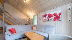 Una sala moderna con un sofá gris claro, una mesa de centro de madera y un sillón blanco. Se ve una escalera al fondo que conduce a un nivel superior.